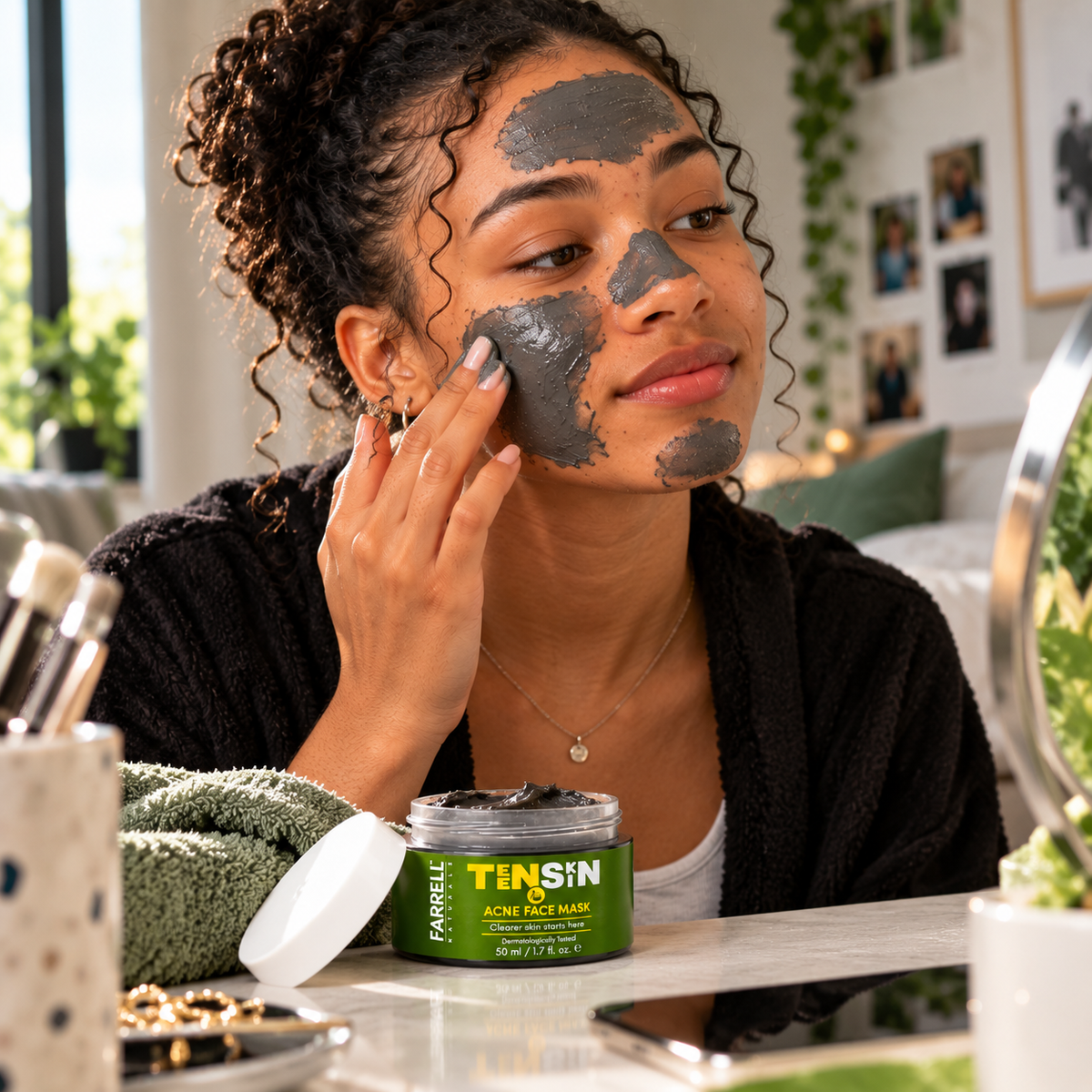 Teenage boy applying a dark face mask while Farrell Naturals Acne Face Mask sits on the bathroom counter.