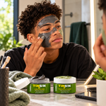 Teenage boy applying a dark face mask with both Farrell Naturals TEENSKIN face mask jars displayed nearby.