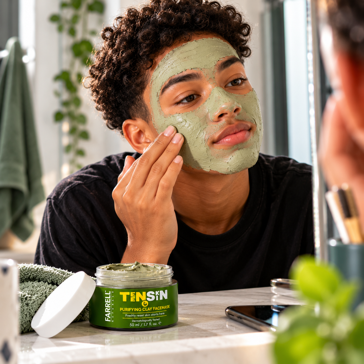 Teenage boy applying a green clay mask while Farrell Naturals Purifying Clay Face Mask sits on the bathroom counter.