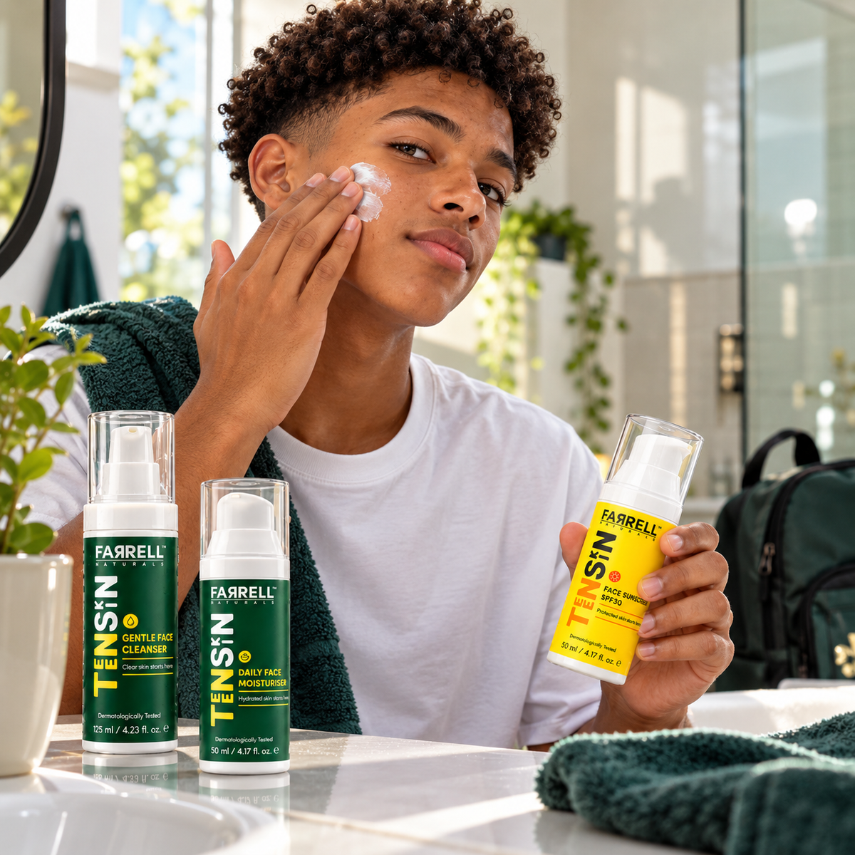 Teenage boy applying skincare with the Farrell Naturals cleanser, moisturiser and sunscreen displayed on the bathroom counter.