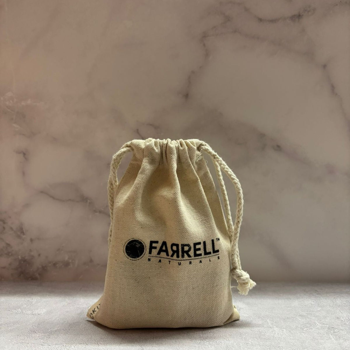 Beige drawstring bag with 'FARRELL' logo on a marble surface